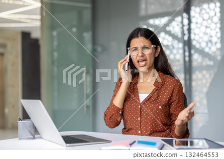Young businesswoman experiencing stress and conflict while making an angry phone call in the office, her expression showing frustration and negative emotion during a heated argument 132464553