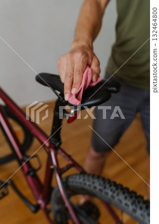 Vertical cropped shot of cyclist cleaning saddle of bicycle with microfiber cloth, performing detailed maintenance after trail riding, close-up. Concept of repair and maintenance of bicycle transport. 132464800