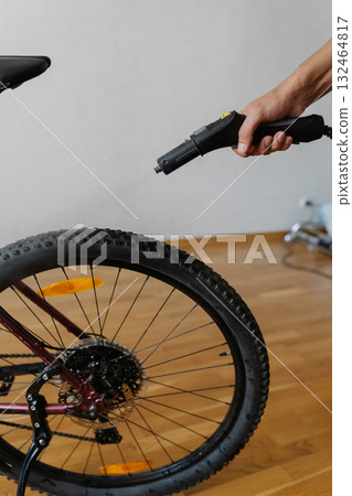 Vertical cropped shot of unrecognizable mechanic male cleaning bicycle tire with steam cleaner, removing dirt and grime for precise maintenance of cycling equipment. Concept of bike maintenance Vertical cropped shot of unrecognizable mechanic male cleaning bicycle tire with steam cleaner, removing dirt and grime for precise maintenance of cycling equipment. Concept of bike maintenance 132464817