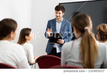 Positive skilled male coach explaining topic to group of people during foreign language class in auditory Positive skilled male coach explaining topic to group of people during foreign language class in auditory 132465017
