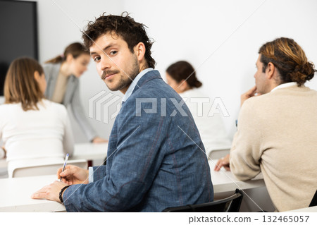 Positive young man turning around and looking at camera during advanced training course in auditory Positive young man turning around and looking at camera during advanced training course in auditory 132465057
