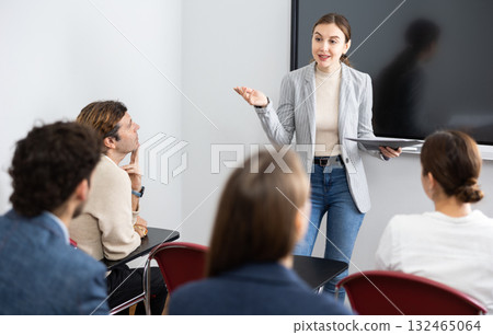 Young woman standing near interactive board and communicating with adult students during advanced training courses in classroom Young woman standing near interactive board and communicating with adult students during advanced training courses in classroom 132465064