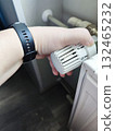 A person adjusts a thermostatic radiator valve with their hand. The valve is attached to a radiator, and the settings range from 1 to 5. 132465232