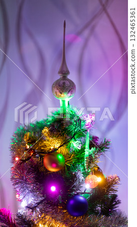 Decorated Christmas tree with colorful lights and ornaments, topped with a festive silver finial. Cozy holiday atmosphere with warm illumination and vibrant celebration mood 132465361