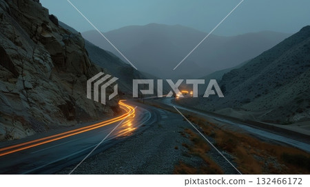 A solitary car makes its way carefully along the narrow mountain highway its headlights casting long trails behind it A solitary car makes its way carefully along the narrow mountain highway its headlights casting long trails behind it 132466172