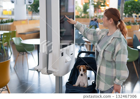 Caucasian woman makes a purchase at a self-service counter with a Jack Russell terrier dog in a stroller in a shopping center. 132467306