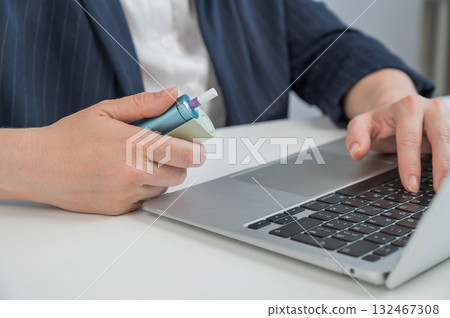 Business woman smoking an electronic cigarette while working on a laptop. Tobacco heating system. Business woman smoking an electronic cigarette while working on a laptop. Tobacco heating system. 132467308