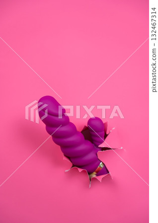 Raspberry sex toy sticks out of pink paper background. Vertical photo. Copy space. Raspberry sex toy sticks out of pink paper background. Vertical photo. Copy space. 132467314