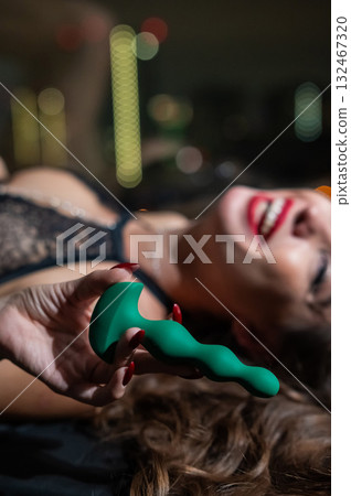 Woman in lace lingerie holding green anal beads.  132467320