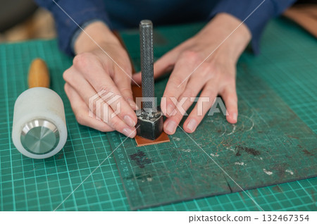 Woman tanner processes the edges of a leather belt in a workshop.  132467354