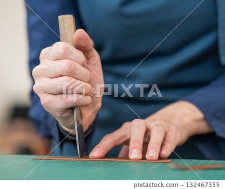 Woman tanner processes the edges of a leather belt in a workshop.  132467355