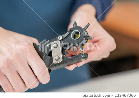 A woman makes holes in a leather belt. Leatherworker's workshop.  132467360