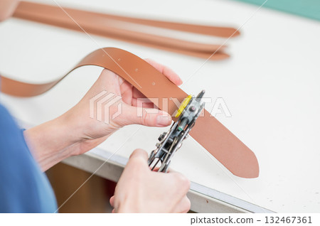 A woman makes holes in a leather belt. Leatherworker's workshop.  132467361