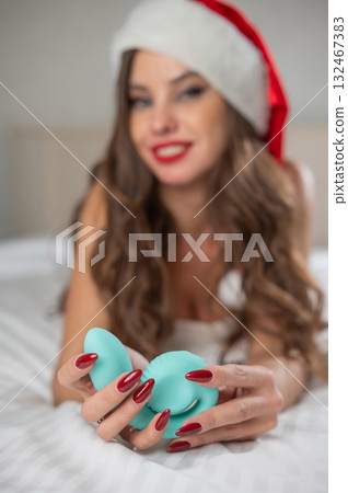 Caucasian woman in Santa Claus costume lying on bed holding curved sex toy.  132467383