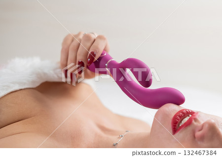 Caucasian woman in Santa Claus costume lying on bed holding curved sex toy. Caucasian woman in Santa Claus costume lying on bed holding curved sex toy. 132467384