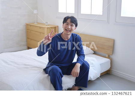 A man in his 20s sitting on a bed making a peace sign 132467621