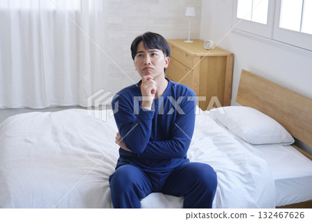 A man in his 20s sitting on a bed thinking A man in his 20s sitting on a bed thinking 132467626