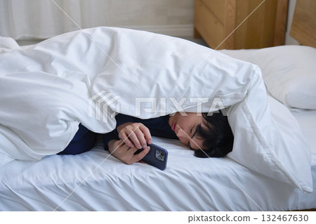 一名 20 多歲的男子裹著被褥使用智慧型手機 132467630
