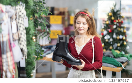 Young woman choosing platform boots on Christmas tree background Young woman choosing platform boots on Christmas tree background 132467917
