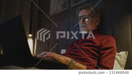 Aged Businessman Works on Laptop in Stylish Hotel Room 132468048