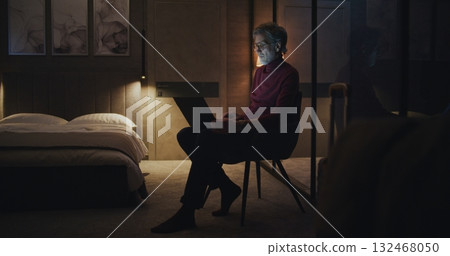 Focused Man Wearing Glasses Types on Laptop in Dimly Lit Hotel Room Focused Man Wearing Glasses Types on Laptop in Dimly Lit Hotel Room 132468050