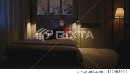 Stylish Senior Businessman Types on His Laptop in Cozy Hotel Room 132468054