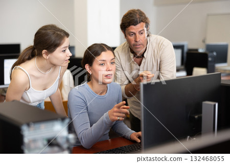 During computer lesson, two companions help girl student complete difficult task 132468055