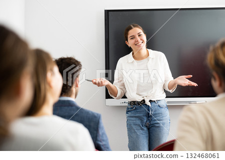 Positive skilled female coach explaining topic to group of people during foreign language class in auditory 132468061