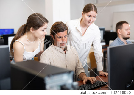 Two female friend companions stands next to computer courses male student 132468090