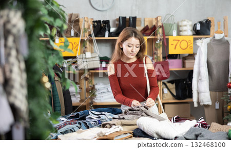 Girl client looks at products in store, looks closely at trousers, picks up wardrobe item Girl client looks at products in store, looks closely at trousers, picks up wardrobe item 132468100