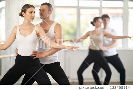 Positive ballet dancers couple performing graceful choreography, training demi plie ballet pose in gym or ballet hall 132468114