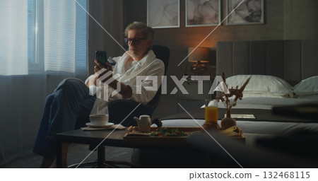 Stylish Senior Man in Soft White Bathrobe Uses Smartphone to Shop Online and Manage Payments Stylish Senior Man in Soft White Bathrobe Uses Smartphone to Shop Online and Manage Payments 132468115