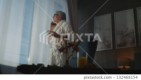 Man in White Hotel Bathrobe Stands By Window, Sipping Tea Man in White Hotel Bathrobe Stands By Window, Sipping Tea 132468154