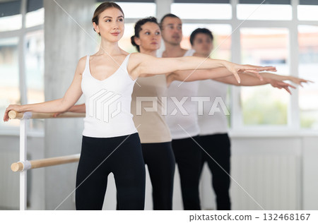 Pretty young girl in black and white sportswear, participating 2nd position of ballet stance at barre with group in choreography studio Pretty young girl in black and white sportswear, participating 2nd position of ballet stance at barre with group in choreography studio 132468167