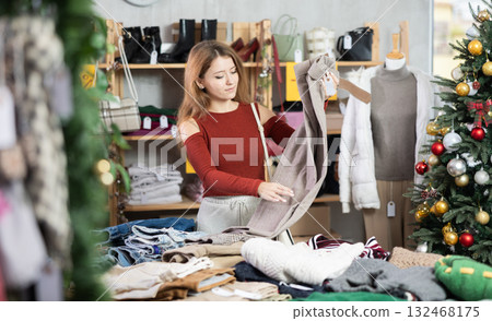 Girl client looks at products in store, looks closely at trousers, picks up wardrobe item 132468175