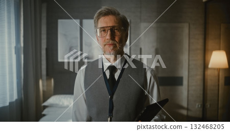 Mature Man in Business Vest and Tie Stands With a Serious, Confident Expression With Gadget in Hands Mature Man in Business Vest and Tie Stands With a Serious, Confident Expression With Gadget in Hands 132468205