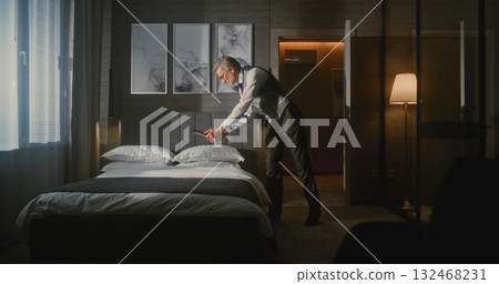 Mature Hotel Manager in Professional Business Attire Meticulously Checks and Photographs Bed 132468231