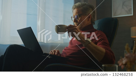 Modern Businessman in Red Turtleneck Enjoys Coffee and Breakfast While Working on Laptop in Hotel Modern Businessman in Red Turtleneck Enjoys Coffee and Breakfast While Working on Laptop in Hotel 132468258