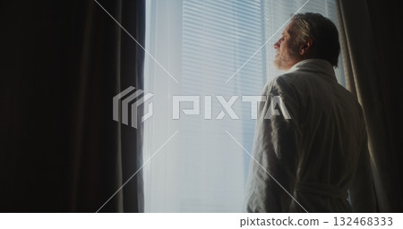 Gray Haired Mature Man Stretches and Opens Window Curtains in Hotel Room as Sunlight Floods in Gray Haired Mature Man Stretches and Opens Window Curtains in Hotel Room as Sunlight Floods in 132468333
