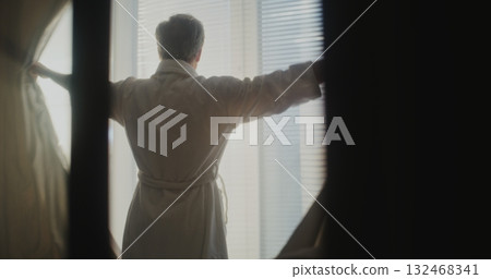 Senior Man Enjoys First Rays of Morning Sun Through Large Hotel Windows Senior Man Enjoys First Rays of Morning Sun Through Large Hotel Windows 132468341