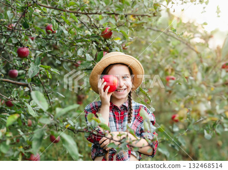 Cheerful girl stands on background an apple orchard with red apples, tastes, enjoys snacks, Cheerful girl stands on background an apple orchard with red apples, tastes, enjoys snacks, 132468514