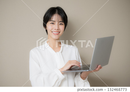 Beautiful pretty dark-haired woman posing with laptop on beige background, looking at camera 132468773