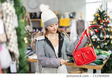 Girl client looks at products in store, looks closely at bag, picks up wardrobe item Girl client looks at products in store, looks closely at bag, picks up wardrobe item 132469000