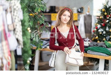 woman in a warm sweater chooses a handbag against the background of a Christmas tree woman in a warm sweater chooses a handbag against the background of a Christmas tree 132469017