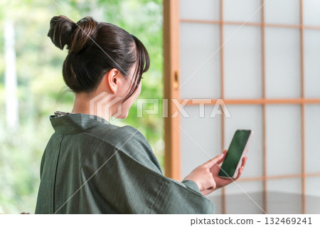 A man in a yukata looking at his smartphone in a Japanese-style room at a ryokan 132469241