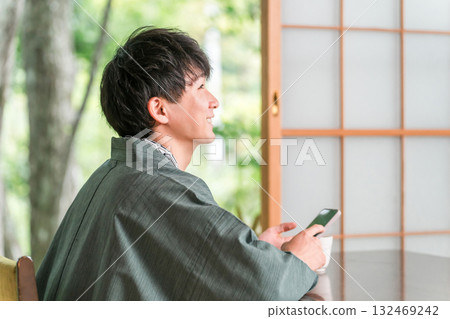 A man in a yukata looking at his smartphone in a Japanese-style room at a ryokan 132469242