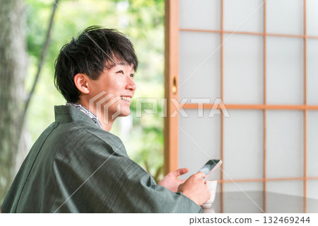 A man in a yukata looking at his smartphone in a Japanese-style room at a ryokan A man in a yukata looking at his smartphone in a Japanese-style room at a ryokan 132469244