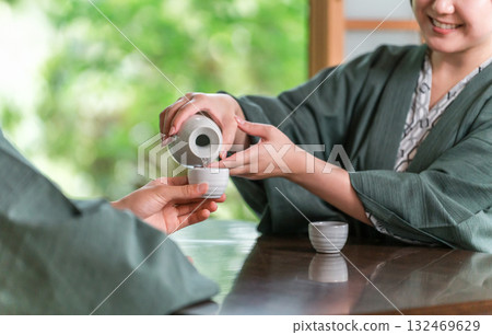The hands of a man and woman in yukata serving drinks in a Japanese-style room at a ryokan 132469629
