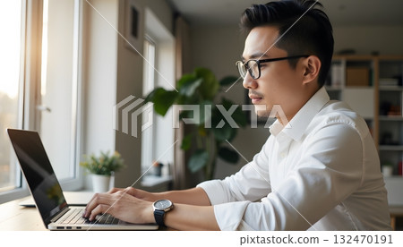 Young man working on laptop in modern office with plant and soft sunlight Young man working on laptop in modern office with plant and soft sunlight 132470191