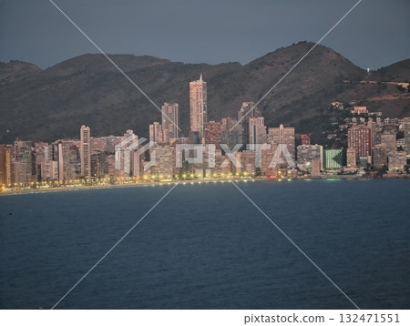 warm evening coastal cityscape, twilight glow reflecting on calm ocean near illuminated walkway 132471551